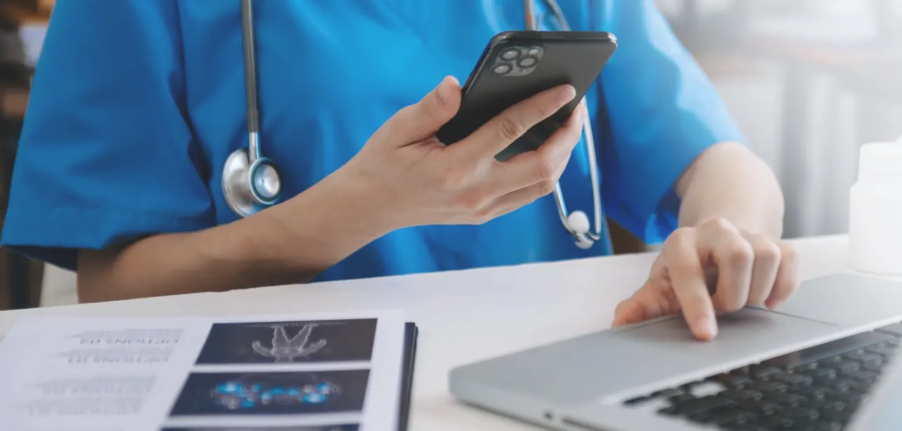 nurse holding phone and operating laptop on desk